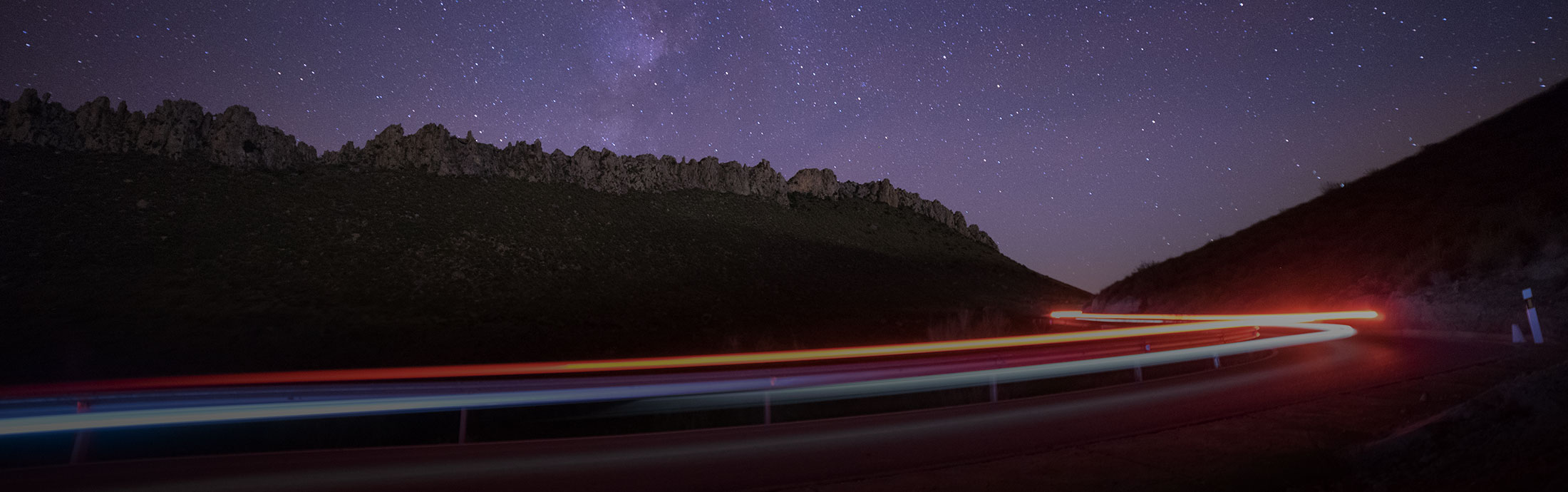 Langzeitbelichtung von Straße bei Nacht mit Sternenhimmel und Wald im Hintergrund